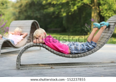 Kids, two boys, twin brothers are chilling out at wooden ergonomic chairs in recreation park