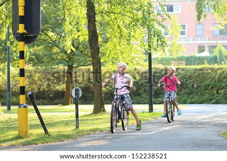Two boys are cycling on their bikes at special training playground in the park, they are learning how to safely cycle in the city by looking at educational traffic signs and stopping at red lights