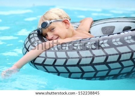 Cute boy swimming in outdoor pool having fun with inflatable ring