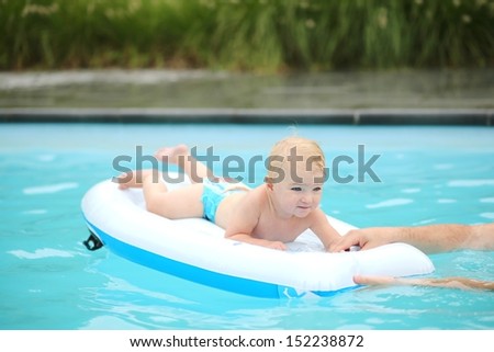 Cute baby plays with water laying on inflatable mattress in outdoors swimming pool