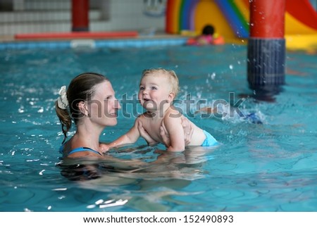 Young beautiful sportive mother teaching cute happy smiling baby to swim in indoors swimming pool