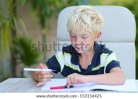 Teenager boy studying home task after school sitting in a garden, he reads and writes