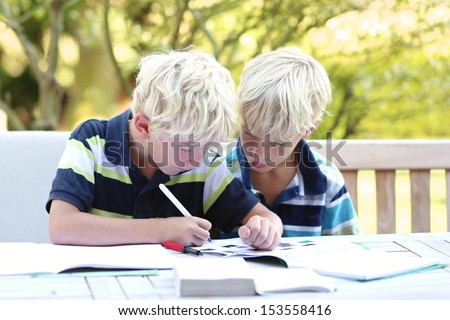 Two cute teenager student boys, twin brothers, are doing together homework sitting after school in the garden, one brother is helping and explaining the other one the task
