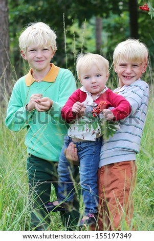 Three happy children, twin brothers with little baby sister walking together in beautiful autumn forest
