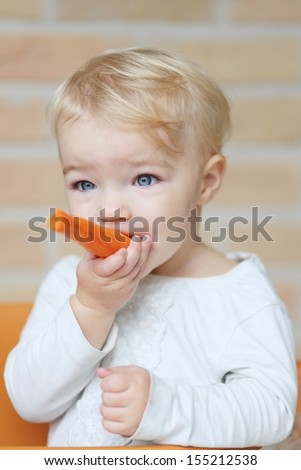 Cute little blond baby girl bites on delicious fresh raw carrot