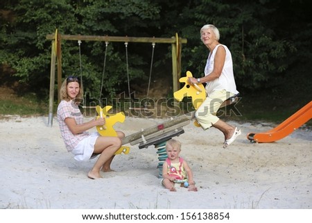 3 generations, a daughter, a mother and a grandmother are having fun on seesaw at a playground