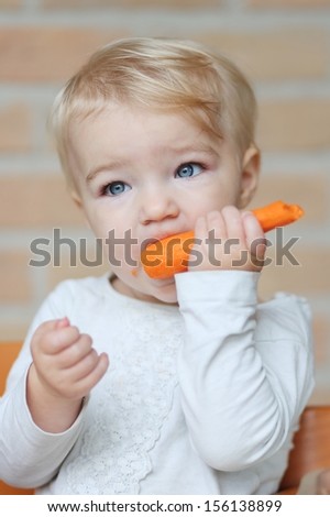Funny little blond baby girl bites on delicious fresh raw carrot