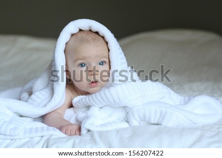 Portrait of cute little newborn baby laying in big bed under worm soft white blanket