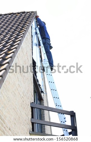 Contractor worker stands on the extension ladder performing task to repair the side of the house under the roof