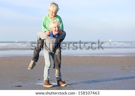 Active laughing teenager boys, twin brothers, having fun playing on the beach on a sunny day