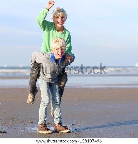 Happy adorable teenager boys, twin brothers, having fun playing on the beach on a sunny day