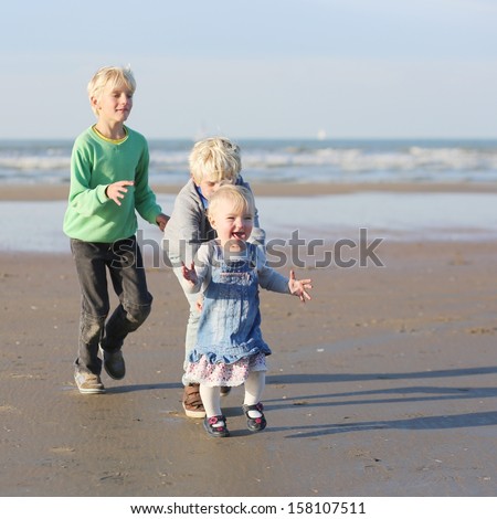 Happy kids, two twin brothers with baby sister, playing and running on the beach on a warm sunny day