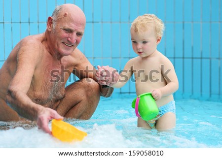 Happy grandfather with grandchild having fun together playing in swimming pool