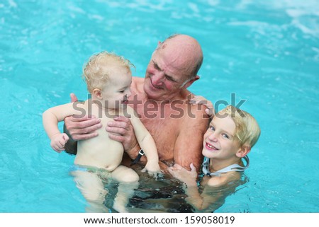 Happy active grandfather with grandchildren having fun together in swimming pool