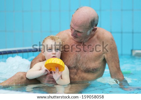 Active grandfather with grandchild having fun together playing in swimming pool