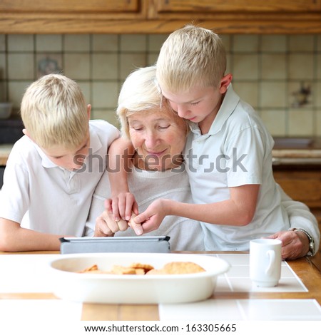 Teenager boys twin brothers teaching grandmother to play on tablet pc, enjoying time together, eating cookies and drinking coffee