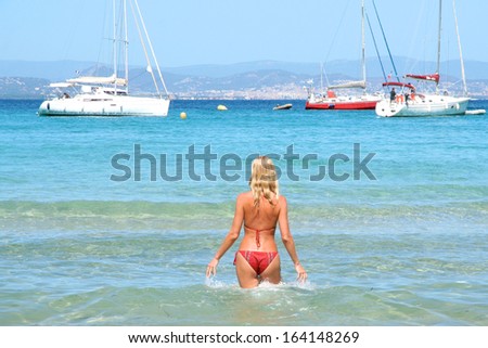 Beautiful young slim woman walking into the sea, white yacht boats at the horizon
