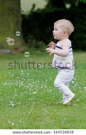 Adorable little girl is playing outdoors trying to catch soap bubbles