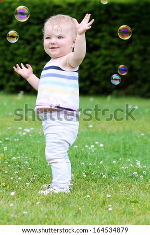 Happy little girl is playing outdoors trying to catch soap bubbles