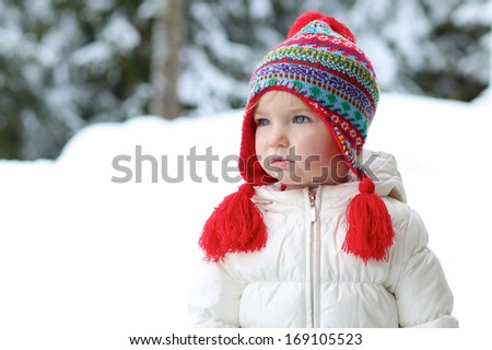 Portrait of cute little toddler girl in beautiful warm outfit playing outdoors in the snow