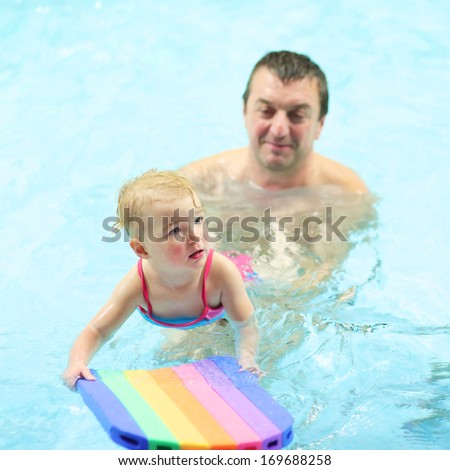Active father teaching his toddler daughter to swim in the pool with floating board