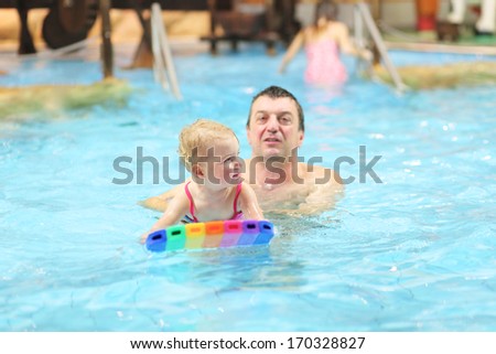 Active father teaching his toddler daughter to swim in the pool with floating board