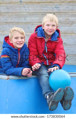 Two happy teenager boys, twin brothers, relaxing after school on the playground playing with ball