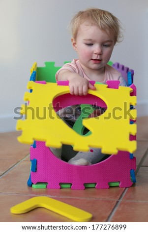 Adorable little toddler girl playing hide and seek and learning numbers with colorful soft puzzles