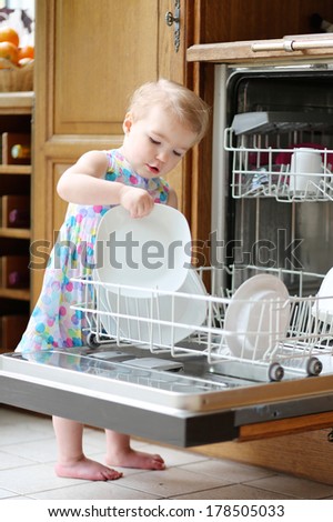 Adorable Smiling Blonde Toddler Girl Helping In The Kitchen Taking Plates Out Of Dish Washing Machine