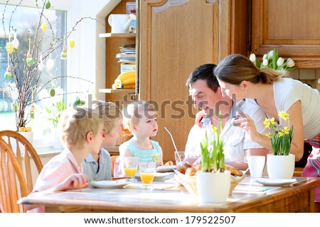 Family of five: father, mother and three kids, teenager sons and toddler daughter eating eggs during family breakfast on Easter day sitting together in sunny kitchen. Selective focus on little girl.