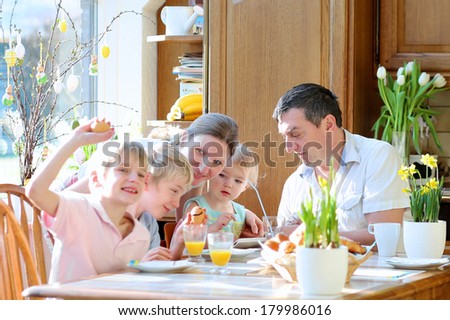 Family of five: father, mother and three kids, teenager sons and toddler daughter eating eggs during family breakfast on Easter day sitting together in sunny kitchen. Selective focus on little girl.