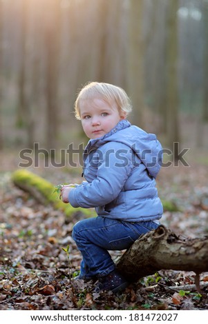 Adorable blonde toddler girl in casual outfit relaxing in the forest on a sunny spring day