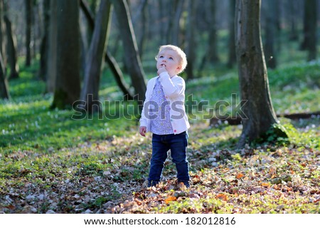 Funny blonde curly toddler girl in casual clothes playing in spring or summer forest on a sunny day