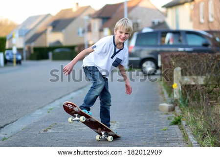 Happy active teenager boy learning to balance on skateboard playing on the street