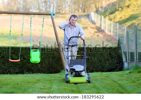 Happy man mowing the lawn in the backyard of his house at the free time on a sunny summer day