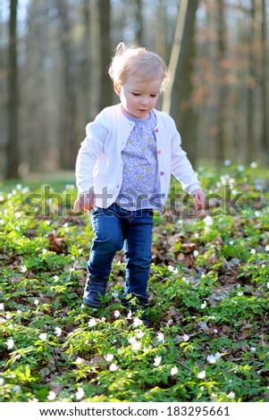 Funny blonde curly toddler girl in casual clothes playing in spring forest on a sunny day