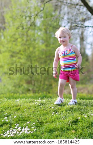 Little child, funny blonde toddler girl, playing in the park jumping on green lawn on a sunny summer day