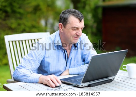 Businessman in casual clothes working from home sitting with laptop outside in the garden - home office concept