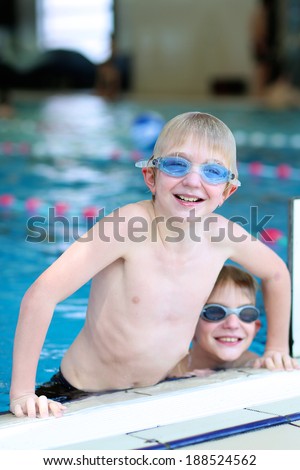 Happy children, twin teenagers boys in swimming goggles, having fun in the pool training before competition