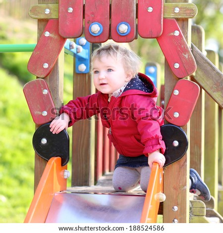 Active child, curly blonde toddler girl having fun in playground on the slide on a sunny day