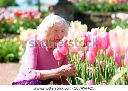 Portrait of happy senior woman next to pink tulips in beautiful spring park - active retirement concept