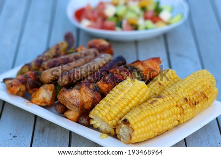 Assorted delicious grilled meat with vegetables on white plate on picnic table for family bbq party