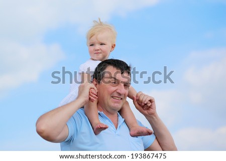 Happy family, a father and his daughter, cute toddler girl with blonde curly hair, enjoying time outdoors, hugging and kissing, on a sunny summer day - blue sky with white clouds at the background
