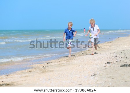 Two happy children, twin brothers, blonde school boys playing on the beach running along the sea shore on a sunny summer day