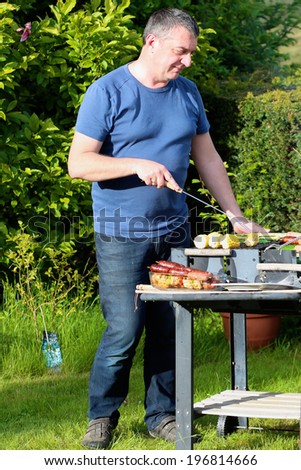 A man preparing delicious assorted meat and vegetables on barbecue grill for summer family party dinner