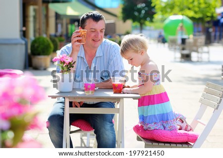 Happy active man relaxing together with his little daughter, adorable blonde toddler girl, in cozy outdoors cafe drinking ice tea and fresh smoothie on a hot summer day - father and child concept