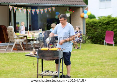 A man cooking meat on barbecue for summer family dinner at the backyard of the house