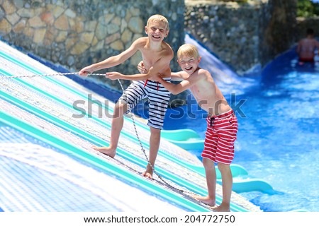 Two happy teenage boys, sportive twin brothers, having fun together jumping in splashing in outdoors swimming pool in aquapark during summer sea vacation
