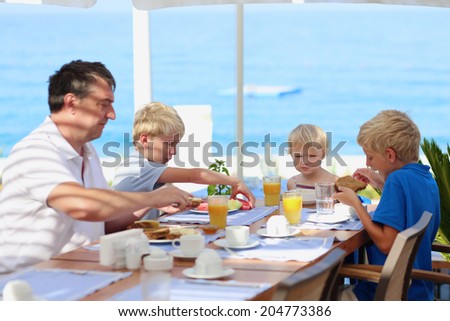 Happy family of four, father with three kids, enjoying summer vacation eating healthy breakfast in the sea view restaurant on tropical resort