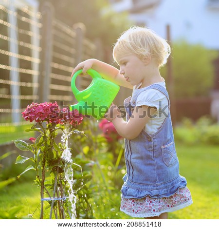 Little child, adorable blonde toddler girl, giving water to the plants, beautiful hortensia flowers, from watering can in the garden at the backyard of the house on a sunny summer evening at sunset